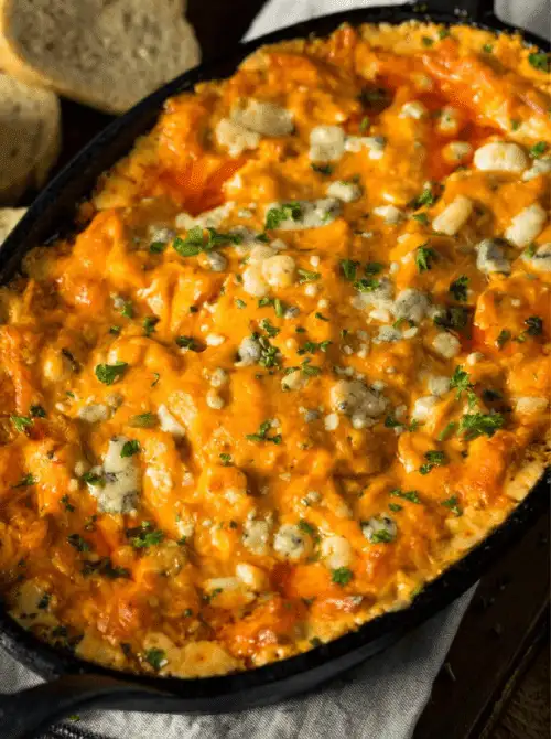 Skillet of creamy buffalo chicken dip topped with blue cheese crumbles and herbs, a great example of easy crock pot recipes for a last minute Super Bowl party.