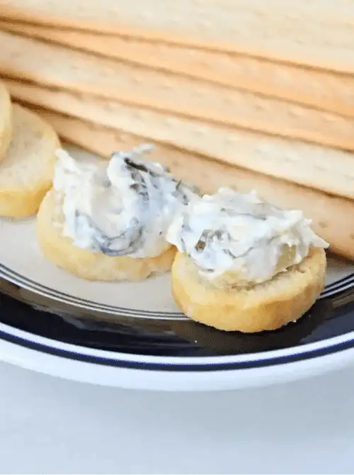 Crackers topped with creamy spinach artichoke dip on a serving plate, part of easy crock pot recipes for a last minute Super Bowl party.