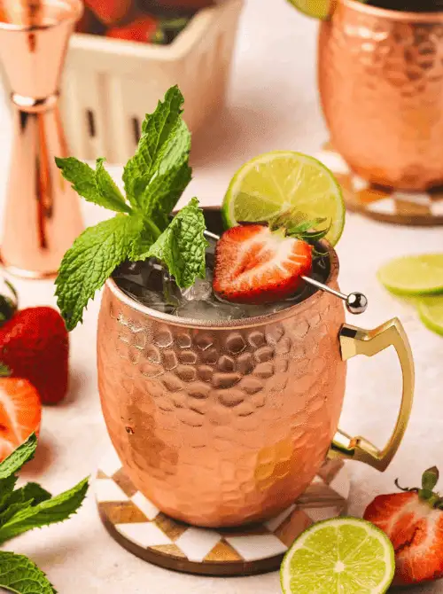 Pink Cocktail Ideas for a Galentine’s Day Party featuring a strawberry Moscow mule served in a copper mug with fresh mint and lime garnishSS