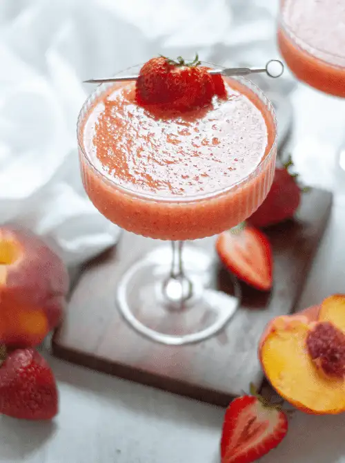 Pink Cocktail Ideas for a Galentine’s Day Party featuring a strawberry peach frosé served in a coupe glass with fresh fruit garnish