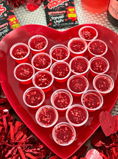Pink Cocktail Ideas for a Galentine’s Day Party featuring strawberry jello shots arranged on a heart-shaped tray with festive toppings
