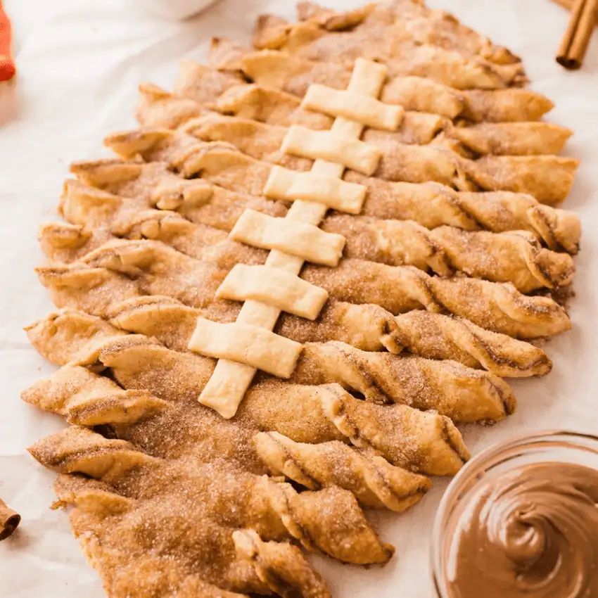 Football-shaped pull-apart dessert bread with cinnamon sugar coating and pastry laces, styled as Super Bowl party food for a football-shaped snack table.