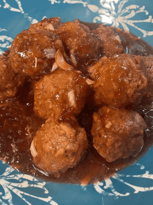 Sweet chili cranberry meatballs simmered in sauce on a blue plate, a fun bite from easy crock pot recipes for a last minute Super Bowl party.