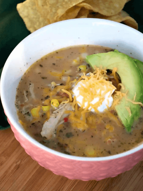 Bowl of creamy white chicken chili topped with cheese and avocado, a cozy option from easy crock pot recipes for a last minute Super Bowl party.