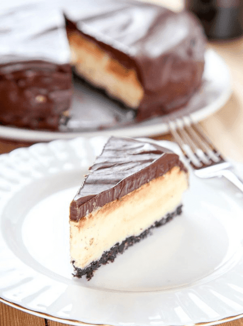 Slice of Bailey’s Irish cream cheesecake with a chocolate topping and cookie crust on a white plate, shown as a make-ahead dessert for St. Patrick’s Day and desserts on a budget.