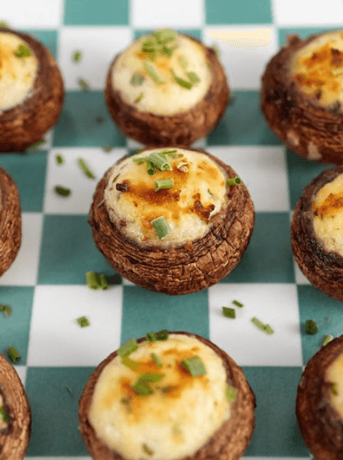 Boursin stuffed mushrooms topped with herbs on a green checkered plate, served as elegant Irish party food for a St. Patrick’s Day celebration.