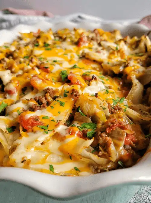 Close-up of cheesy baked cabbage and ground beef casserole with tomatoes and fresh herbs, a cozy choice for super easy casseroles and comforting family dinner ideas.