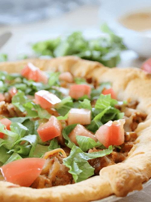 Taco crescent roll casserole topped with fresh lettuce and diced tomatoes in a golden crust, a flavorful option for super easy casseroles and crowd-pleasing family dinner ideas.