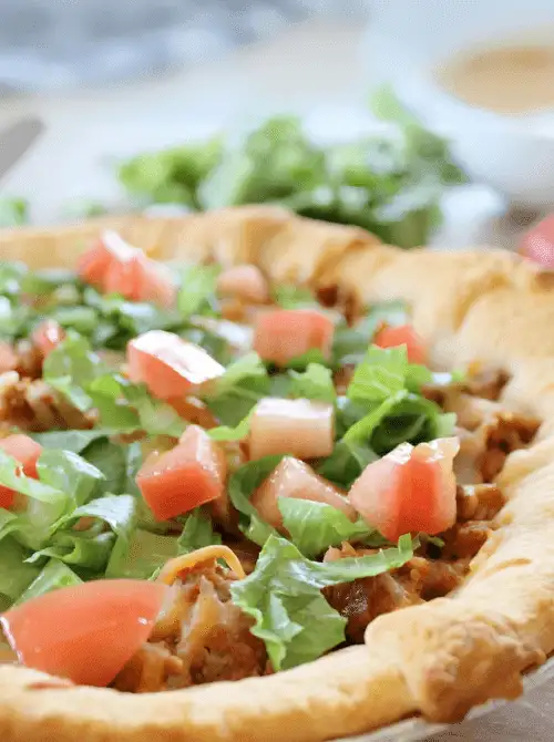 Taco crescent roll casserole topped with fresh lettuce and diced tomatoes in a golden crust, a flavorful option for super easy casseroles and crowd-pleasing family dinner ideas.