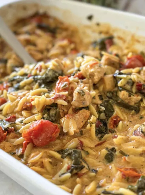Baked chicken orzo casserole with tender chicken pieces, tomatoes, spinach, and creamy sauce in a white baking dish, a flavorful option among chicken casseroles for easy weeknight dinners.