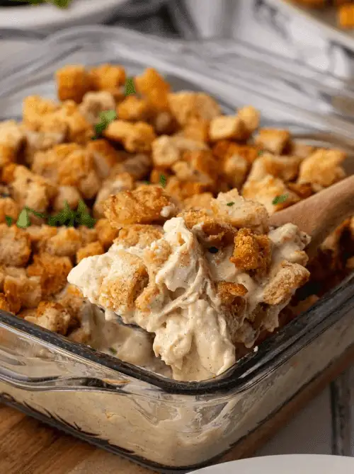 Spoonful of creamy chicken and stuffing casserole with golden bread cubes in a glass baking dish, representing comforting chicken casseroles for easy weeknight dinners.