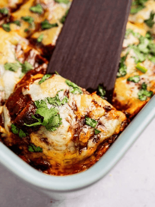 Close-up of cheesy baked enchilada casserole being lifted from a baking dish with a spatula, a flavorful example of super easy casseroles and satisfying family dinner ideas.