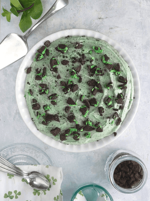 Mint Oreo no-bake pie topped with crushed cookies on a white pie plate, festive St. Patrick’s Day dessert on a budget.