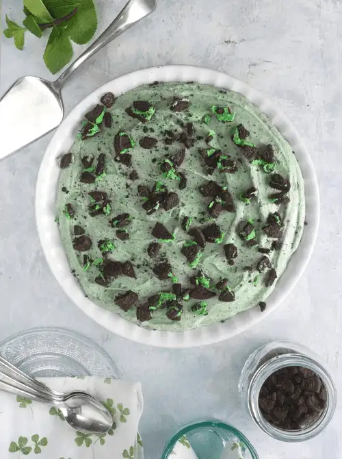Mint Oreo no-bake pie topped with crushed cookies on a white pie plate, festive St. Patrick’s Day dessert on a budget.