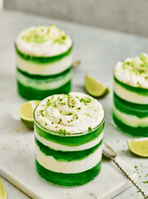 Individual green and white layered dessert parfaits topped with whipped cream and lime zest, served as make-ahead desserts for St. Patrick’s Day and desserts on a budget.