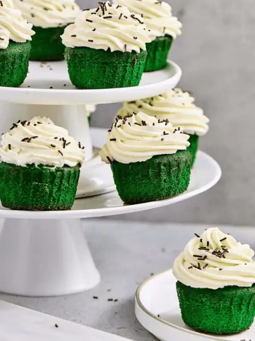 Tiered display of green cupcakes with vanilla buttercream and chocolate sprinkles arranged for an elegant St. Patrick’s Day Dessert Ideas buffet table.