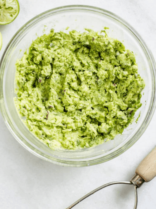 Creamy green guacamole in a glass bowl with lime, a fresh Irish party food dip option for a St. Patrick’s Day celebration.