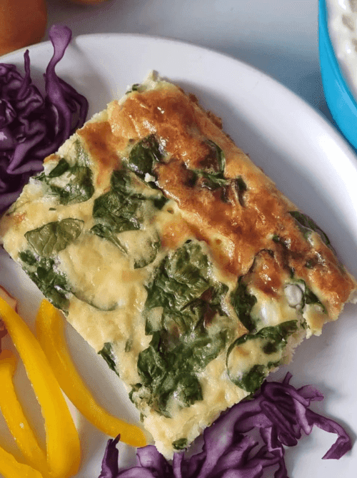 Slice of vegetable egg casserole with spinach and zucchini served on a white plate with fresh veggies, a lighter option among super easy casseroles and wholesome family dinner ideas.
