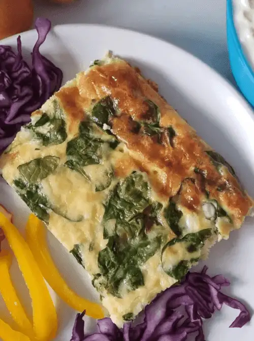 Slice of vegetable egg casserole with spinach and zucchini served on a white plate with fresh veggies, a lighter option among super easy casseroles and wholesome family dinner ideas.