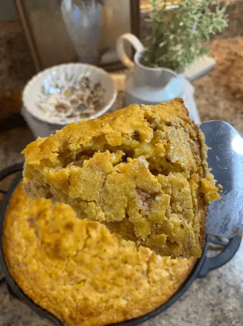 Slice of Jiffy cornbread casserole with tomatoes and okra lifted from a cast iron skillet, a budget-friendly example of super easy casseroles and comforting family dinner ideas.