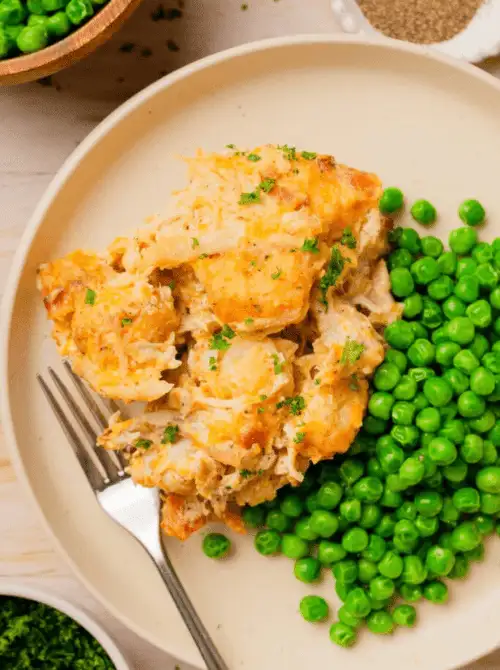 Plated serving of cheesy chicken casserole topped with herbs and served alongside green peas, a simple example of chicken casseroles for easy weeknight dinners.