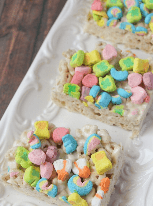 Lucky Charms marshmallow cereal bars topped with colorful marshmallows arranged on a platter, featured in playful St. Patrick’s Day Dessert Ideas for a kid-friendly party table. 🍀
