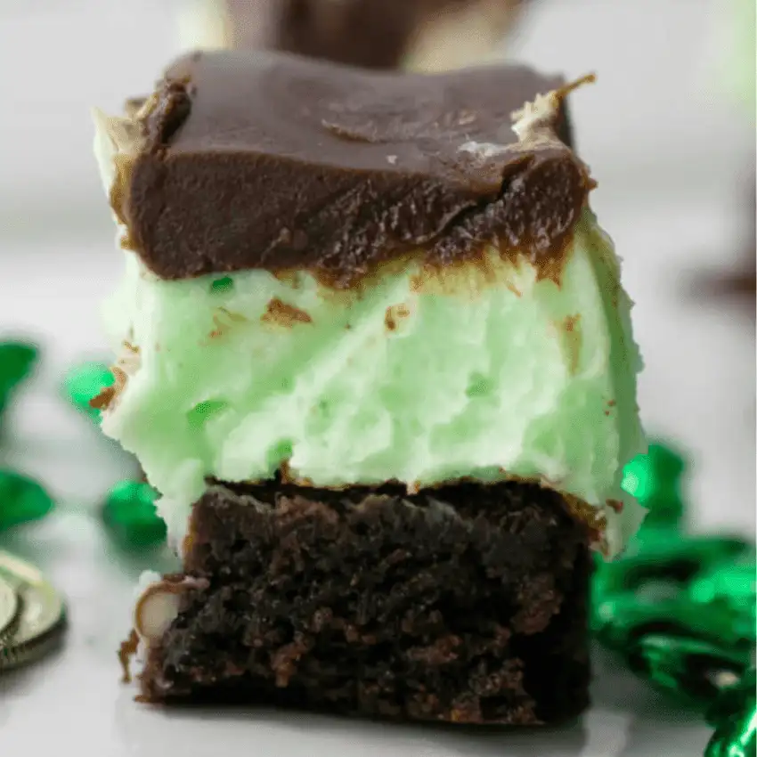 Close-up of a chocolate brownie bar layered with green mint cream and chocolate glaze, a make-ahead dessert for St. Patrick’s Day that fits desserts on a budget.