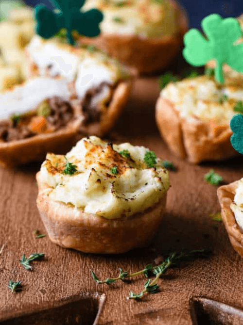 Mini shepherd’s pies topped with mashed potatoes and herbs, served as comforting Irish party food for a St. Patrick’s Day celebration.