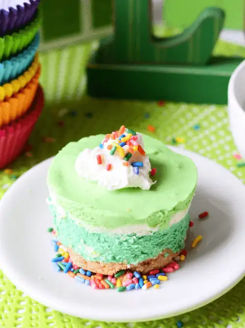 Mini green no-bake cheesecake topped with whipped cream and rainbow sprinkles, a make-ahead dessert for St. Patrick’s Day that works well for desserts on a budget.