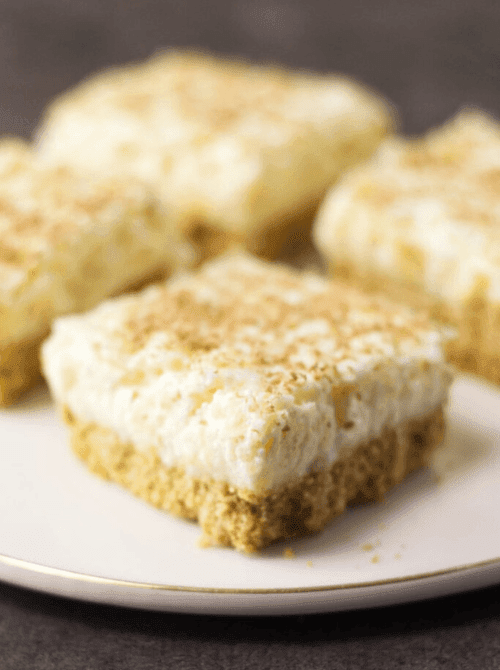 Pineapple delight dessert bars with a crumb crust and creamy topping on a plate, shown as make-ahead desserts for St. Patrick’s Day and desserts on a budget.