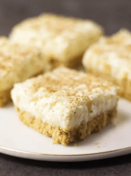 Pineapple delight dessert bars with a crumb crust and creamy topping on a plate, shown as make-ahead desserts for St. Patrick’s Day and desserts on a budget.