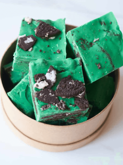 Green mint Oreo fudge squares stacked in a small bowl, an easy make-ahead dessert for St. Patrick’s Day that fits desserts on a budget.