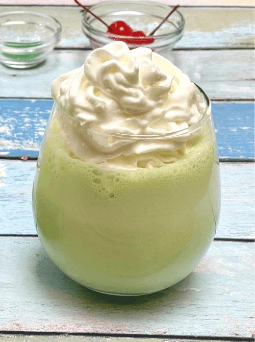 Pale green shamrock shake topped with whipped cream in a clear glass, an easy no-bake St. Patrick’s Day dessert.