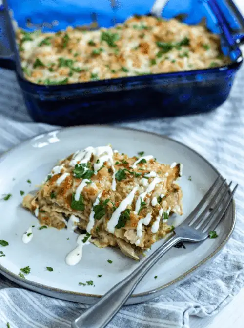 Slice of creamy layered casserole drizzled with sauce and fresh herbs on a plate, with the baking dish in the background, showcasing super easy casseroles and comforting family dinner ideas.