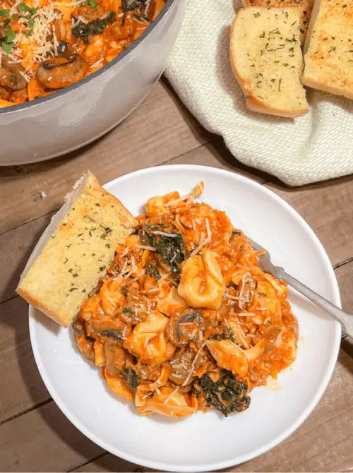Bowl of creamy chicken tortellini casserole with tomato sauce, spinach, and mushrooms served with garlic bread, a hearty example of chicken casseroles for easy weeknight dinners.