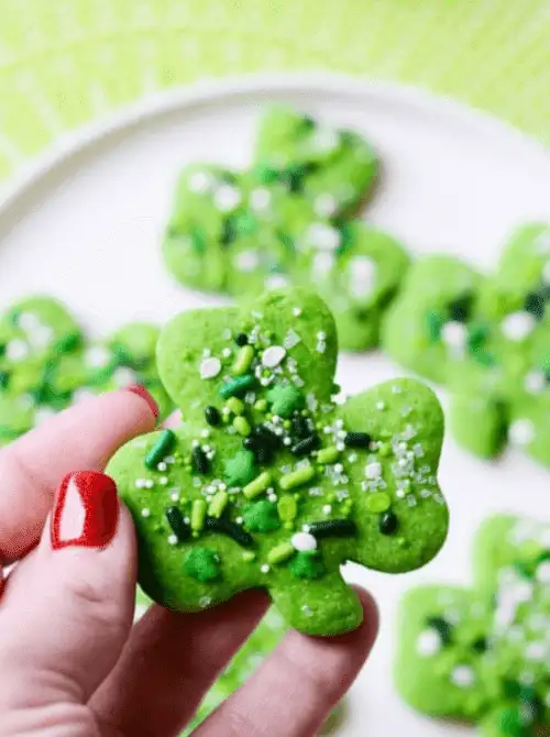 Hand holding a soft green shamrock cookie topped with festive sprinkles, featured in creative St. Patrick’s Day Dessert Ideas for a fun party table.