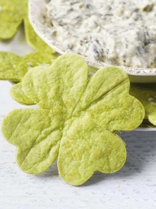 Shamrock-shaped green tortilla chips served with creamy dip, a festive Irish party food option for a St. Patrick’s Day celebration.