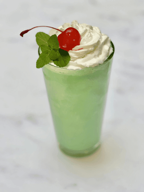 Green mint milkshake with whipped cream and cherry garnish, simple St. Patrick’s Day party treat.