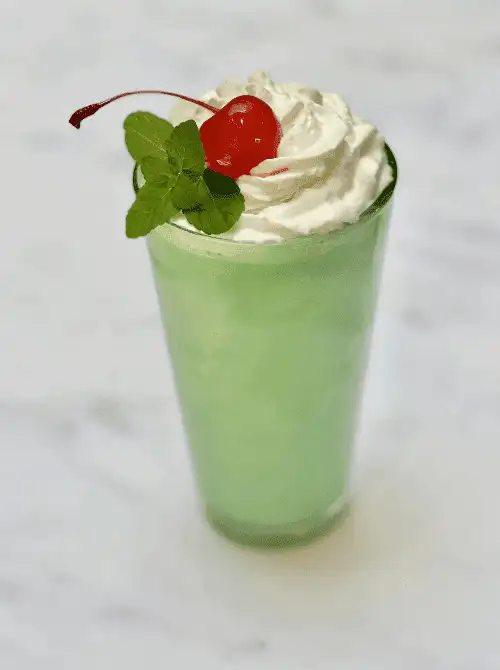 Green mint milkshake with whipped cream and cherry garnish, simple St. Patrick’s Day party treat.