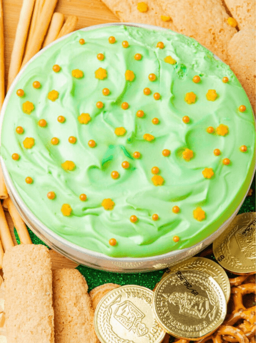 Creamy green dessert dip topped with gold sprinkles and shamrock confetti, surrounded by cookies and pretzels for festive St. Patrick’s Day Dessert Ideas at a party table. 🍀