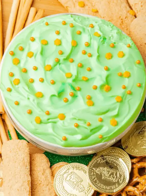 Creamy green dessert dip topped with gold sprinkles and shamrock confetti, surrounded by cookies and pretzels for festive St. Patrick’s Day Dessert Ideas at a party table. 🍀