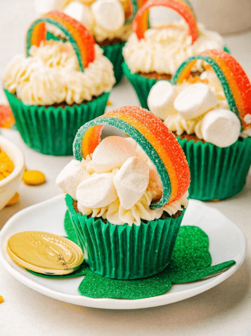 Rainbow-topped cupcakes with marshmallows and green liners styled for a festive St. Patrick’s Day Dessert Ideas table, featuring gold coin accents and playful candy details.
