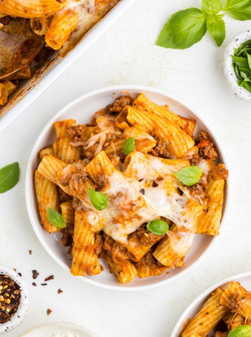 Cheesy rigatoni pasta casserole with ground beef, tomato sauce, and fresh basil served in a bowl, a delicious comfort casseroles option for easy comfort food and recipes for busy nights.