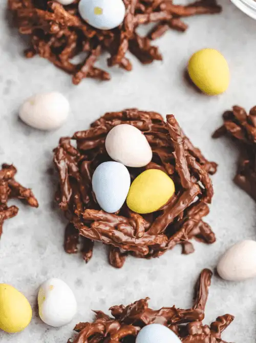 Chocolate bird nest treats made with crunchy noodles and topped with pastel candy eggs, a classic no-bake Easter-themed dessert for a bake sale.