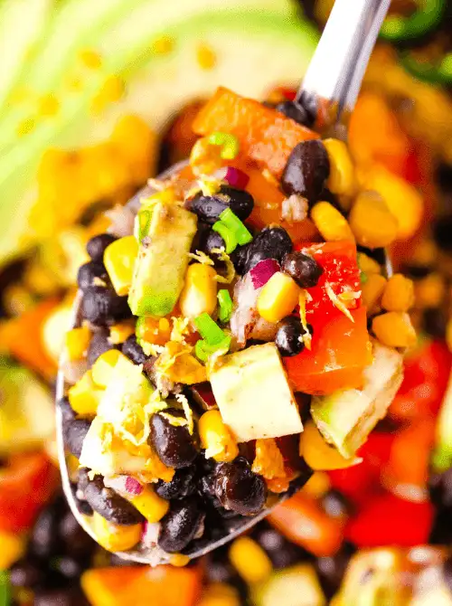 Easy Cinco de Mayo party food recipes for a crowd featuring a close-up spoonful of colorful black bean salad with corn, avocado, tomatoes, and fresh herbs.