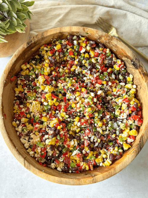Black bean and corn dip with feta in a large wooden bowl with red bell pepper, jalapeño, and cilantro — an easy Cinco de Mayo party food recipe for a crowd that's ready in just 10 minutes.