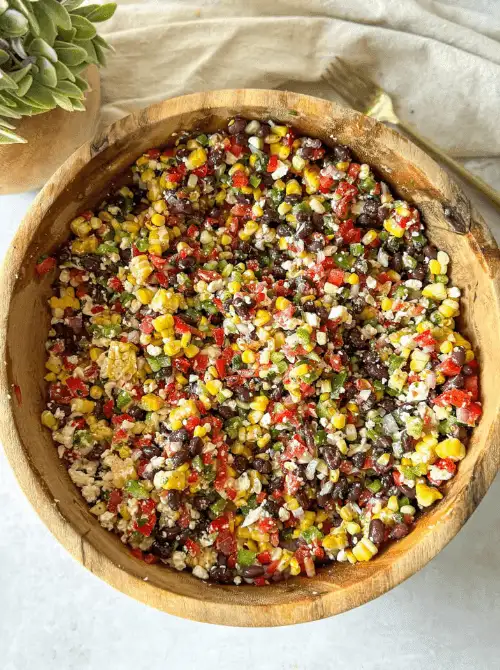 Black bean and corn dip with feta in a large wooden bowl with red bell pepper, jalapeño, and cilantro — an easy Cinco de Mayo party food recipe for a crowd that's ready in just 10 minutes.