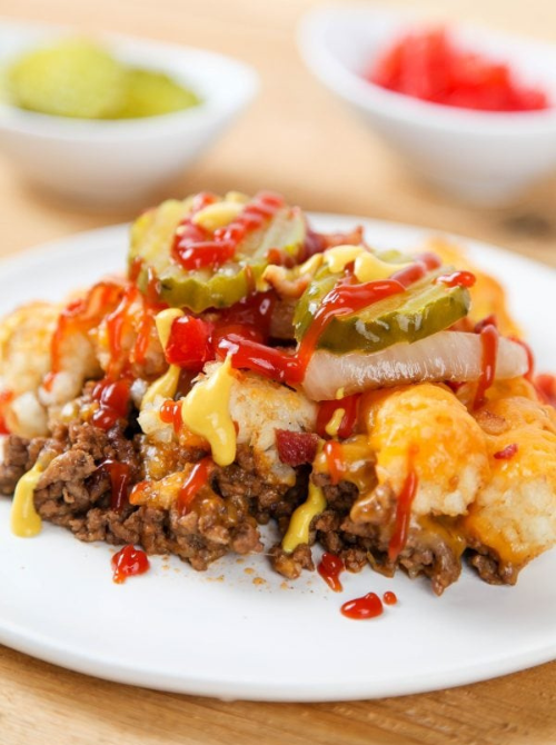 Loaded tater tot casserole topped with ground beef, melted cheese, pickles, onions, and drizzled sauces, a bold comfort casseroles dish for easy comfort food and recipes for busy nights.