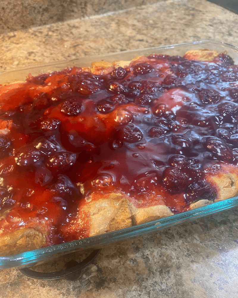 Baked Cherry Cheesecake Monkey Bread Casserole in a glass 9x12 baking dish, topped with glossy cherry pie filling over golden cinnamon-sugar biscuit pieces.