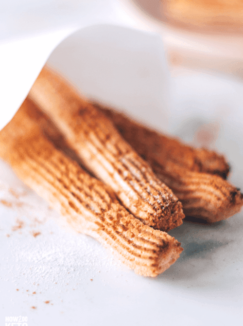 Baked keto churros dusted with cinnamon sugar on a white surface — a gluten-free easy Cinco de Mayo party food recipe for a crowd that makes 14 low-carb churros at just 65 calories each.